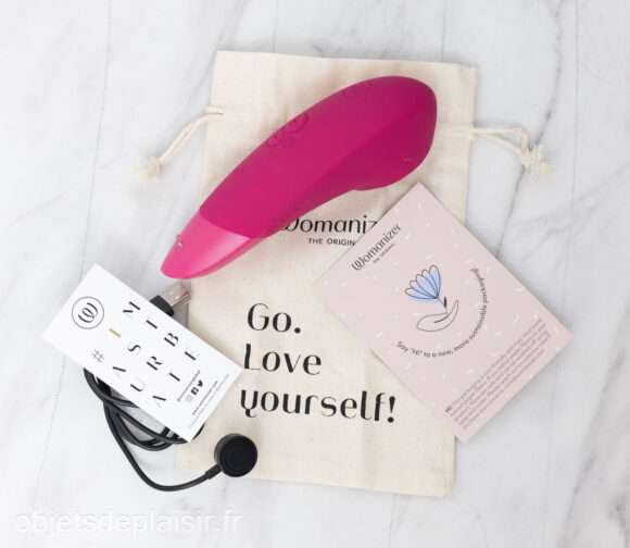 Le Womanizer Enhance, son étui, son câble de chargement et sa notice d'utilisation